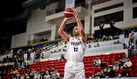 Basketball player in white uniform with number 12, holding a red basketball, in an indoor stadium.